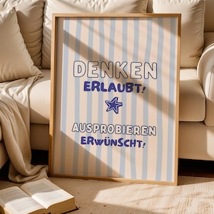 Könnte beinhalten: Ein gerahmtes vertikales Poster mit hellbeigem Hintergrund und vertikalen hellblauen Streifen. Der Text "DENKEN ERLAUBT!" steht über einem blauen Sternsymbol, gefolgt von dem Text "AUSPROBIEREN ERWÜNSCHT!" in einer fetten, dunkelblauen Schrift.