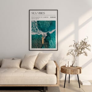 May include: A framed print with the text "SEA VIBES" and "PHOTOGRAPHY OF A SURFER FROM ABOVE" in black text. The image shows a surfer on a surfboard in the ocean, photographed from above. The text "HAWAII" is in the top right corner.