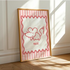 May include: Framed print with a red cartoon mouse illustration. The artwork has a white background with pink vertical stripes and a wavy pink border. The word "MAUSIG" is written below the mouse. The frame is wooden.