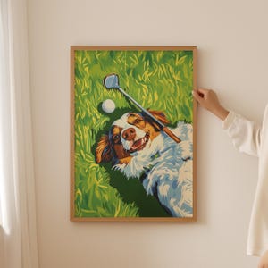 May include: A framed print featuring a happy dog lying in green grass, holding a golf club. A golf ball rests nearby. The dog has brown, white, and black fur. The artwork is in a wooden frame.