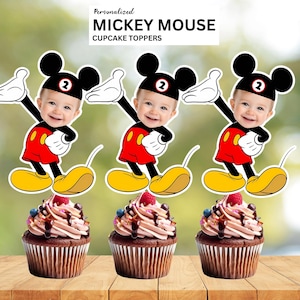 May include: Three Mickey Mouse cupcake toppers with a baby's face, red shorts, yellow shoes, and white gloves. The cupcakes have chocolate frosting, berries, and chocolate drizzle. The text at the top says "Personalized MICKEY MOUSE CUPCAKE TOPPERS."