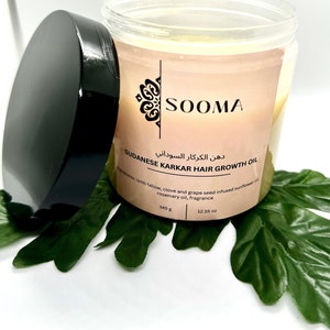 Op de afbeelding: Een glazen pot met een zwarte deksel gevuld met gele olie. Het etiket vermeldt "SOOMA", "دهن الكركار السوداني", "SUDANESE KARKAR HAIR GROWTH OIL", "Ingrediënten: lamsvet, kruidnagel en druivenpitolie geinfuseerd in zonnebloemolie, rozemarijnolie, geur", "345 g" en "12.16 oz".