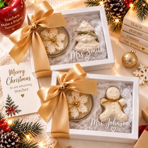 May include: Two white gift boxes containing a snowflake candle and a holiday-shaped wax melt. One box features a white Christmas tree wax melt labeled Mrs. Smith, and the other a gingerbread man wax melt labeled Mrs. Johnson, both tied with gold ribbons.