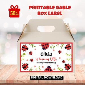 May include: A white gable box with a ladybug-themed label. The label features red ladybugs, green leaves, and the text "Olivia is turning ONE." The box also has the text "Printable Gable Box Label" and "Digital Download."