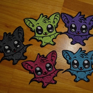May include: Five embroidered iron-on patches of cute cartoon bats in different colors: black, green, purple, pink, and blue. Each bat has large eyes and a smiling mouth.