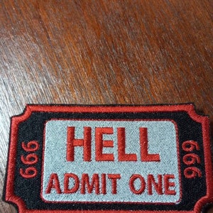 May include: A black and red embroidered patch shaped like a ticket with the text "HELL ADMIT ONE" and the number "666" on each side.