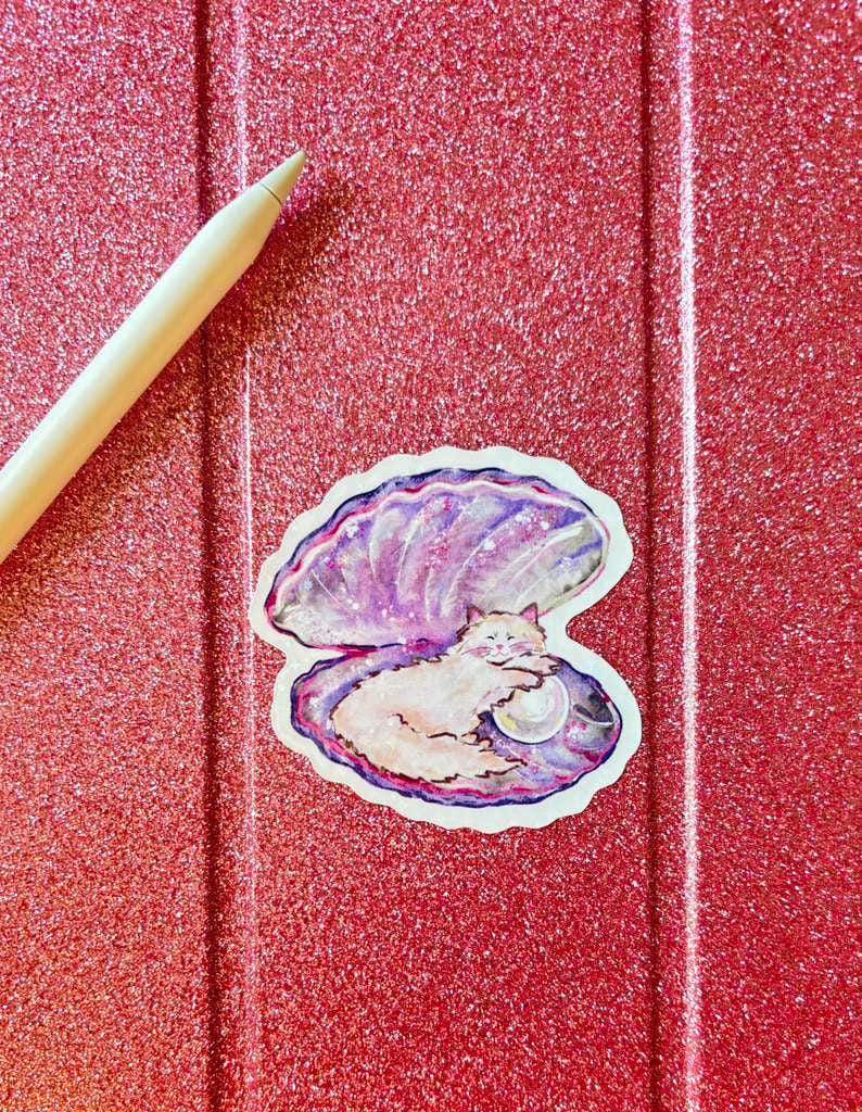 May include: A sticker depicting a white cat nestled in a purple and blue seashell, with a pearl. The sticker is on a red glittery surface, with a light-coloured stylus in the upper left corner.