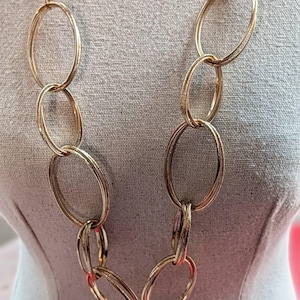 May include: A gold-coloured necklace featuring large oval links. The necklace is displayed on a mannequin. The chain is made of connected oval rings. A statement piece of jewellery.