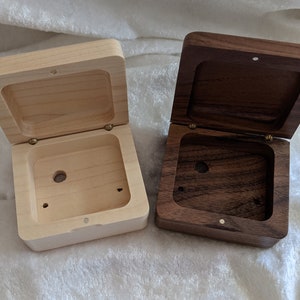 May include: Two wooden boxes with lids open. The box on the left is made of light wood and the box on the right is made of dark wood.