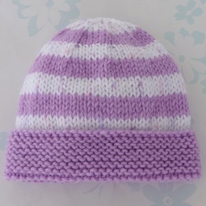 Peut inclure: Un bonnet tricoté à rayures horizontales blanches et lilas. Le bord est de couleur lilas uni. Le chapeau est fait de fil doux et convient aux bébés ou aux enfants.