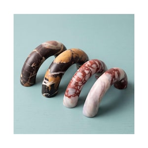 Puede incluir: Cuatro tiradores de armario arqueados hechos de piedra pulida, cada uno con un patrón veteado natural único. El conjunto incluye un acabado de mármol en marrón oscuro, negro y dorado, rojo intenso y blanco, y rosa pálido y blanco.