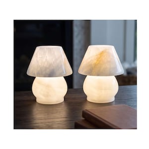 May include: Two mushroom-shaped table lamps crafted from translucent white stone with visible natural veining. Each lamp features a rounded base and a wide, conical shade that emits a soft, warm glow, highlighting the unique texture of the stone material.