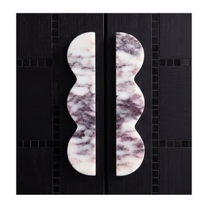 Puede incluir: Dos tiradores de armario verticales hechos de mármol blanco con vetas púrpuras, con un diseño de borde festoneado. Los tiradores están montados uno al lado del otro en una puerta de armario negra con textura de rejilla y azulejos.