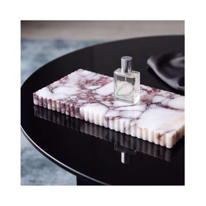 May include: A rectangular white marble tray with deep purple veining and a fluted, scalloped edge design. A small, clear glass perfume bottle with a silver cap sits on the surface of the tray, which has a polished and smooth finish.
