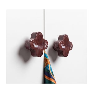 May include: Two dark reddish-brown marble cabinet knobs with a four-lobed clover shape attached to a white surface. A portion of a patterned silk scarf with blue, green, and orange colours hangs between the two knobs on the white cabinet doors.