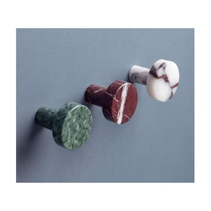 Può includere: Tre pomelli circolari in pietra naturale, ognuno caratterizzato da un colore e una venatura distinti. Un pomello è verde scuro, uno è rosso intenso con venature bianche e uno è bianco con venature viola scuro, montati su una superficie.