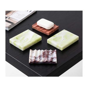 May include: Two rectangular soap dishes with a light green and white marbled pattern, one reddish-brown corrugated soap dish holding a white bar of soap, and one white and dark purple marbled corrugated soap dish with a wavy surface design.