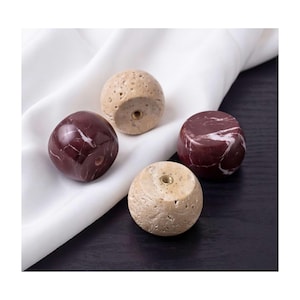 Peut inclure: Quatre boutons de placard sphériques présentant deux textures et couleurs distinctes. Deux boutons sont en pierre bordeaux lisse et polie avec des veines blanches, tandis que les deux autres sont en pierre beige poreuse et texturée.