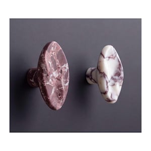 May include: Two oval-shaped cabinet knobs with a polished finish. One knob features a deep burgundy and white marbled stone pattern, while the other knob displays a creamy white base with prominent dark purple veining throughout the surface.
