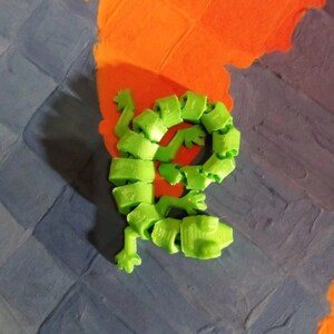 May include: A green, segmented, articulated toy lizard with a curled tail. The toy is made of plastic and has a bright green color.
