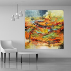 May include: Large abstract artwork in shades of orange, yellow, red, and blue. The painting hangs on a white wall above a small round table and a white chair. The artwork has a textured finish, creating a dynamic visual effect.