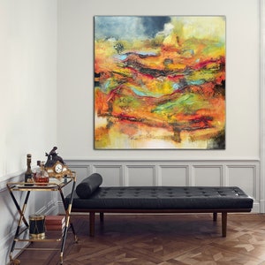 May include: Large abstract painting in shades of orange, yellow, red, and blue. The artwork hangs on a white wall above a black leather daybed. A gold and black drinks trolley with bottles and a clock is in the foreground.