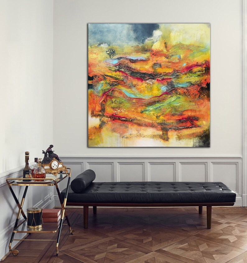May include: Large abstract painting in shades of orange, yellow, red, and blue. The artwork hangs on a white wall above a black leather daybed. A gold and black drinks trolley with bottles and a clock is in the foreground.