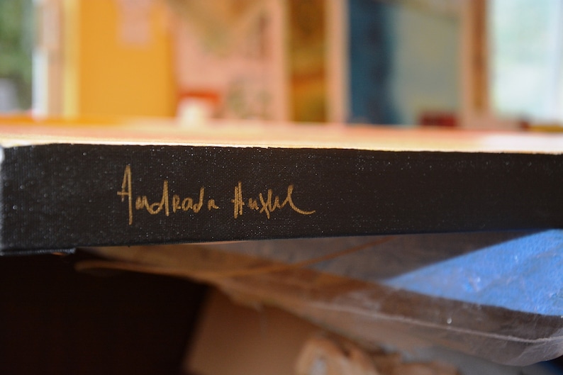 May include: Detail of a canvas artwork with a black border. The artist's signature, "Andrada Hustul," is inscribed in gold script on the side. The painting's colours are visible in the background.