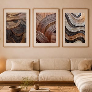 Puede incluir: Un conjunto de tres láminas de arte mural enmarcadas con pinceladas abstractas, gruesas y texturizadas en tonos marrón, negro y crema. Cada lámina rectangular está enmarcada en madera clara y muestra líneas curvas, superpuestas y fluidas.