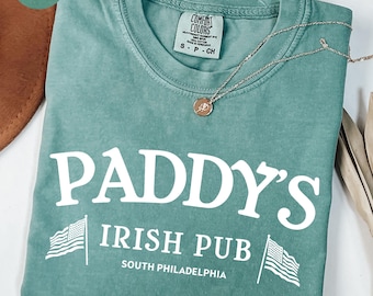 May include: A light green t-shirt with the text "Paddy's Irish Pub South Philadelphia" and two American flags on either side of the text. The shirt is made of a soft, comfortable material.