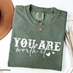 May include: A green t-shirt with the text "YOU ARE worth it" in white with a distressed look. Two small white hearts are to the right of the text.