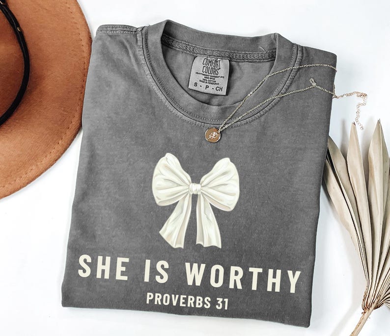 May include: Gray t-shirt with a white bow and the text "SHE IS WORTHY PROVERBS 31" printed on the front.