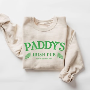 May include: A beige sweatshirt with the text "Paddy's Irish Pub South Philadelphia" and two green shamrock flags on either side of the text.
