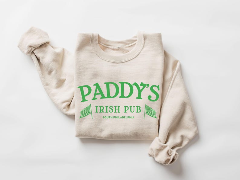 May include: A beige sweatshirt with the text "Paddy's Irish Pub South Philadelphia" and two green shamrock flags on either side of the text.