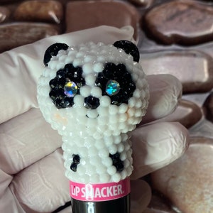 May include: A black Lip Smacker lip balm tube with a white and black panda bear design. The panda bear is covered in rhinestones.