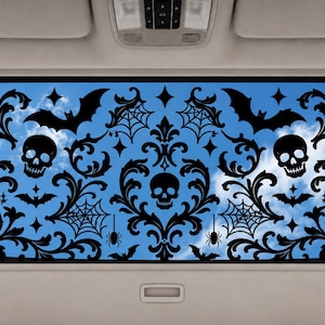 May include: A black vinyl decal applied to a car sunroof, featuring a repeating damask pattern with skulls, flying bats, spider webs, and small spiders. The intricate black design contrasts against the blue sky visible through the glass.