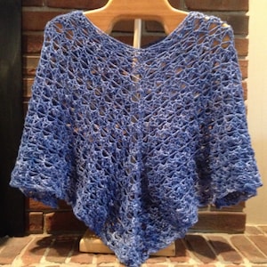 May include: A blue crocheted shawl with a lacy pattern. The shawl is draped over a wooden hanger and is hanging in front of a brick wall.