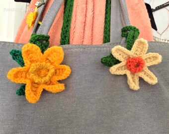 May include: A gray tote bag with two crocheted flower embellishments. One flower is yellow and the other is cream with an orange center.