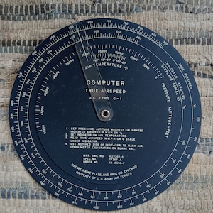 May include: A black circular aircraft computer for calculating true airspeed. The computer has a dial with markings for pressure altitude, indicated airspeed, true airspeed, and air temperature. The text "COMPUTER TRUE AIRSPEED AC. TYPE G-I" is printed on the face of the computer. The text "MFR. DWG. NO. A 22262-A SPEC. NO. 27367-A ORDER NO. 42-18050-P CROWE NAME PLATE AND MFG. CO. CHICAGO PROPERTY OF U.S. ARMY AIR FORCES" is printed on the back of the computer.