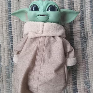 May include: A green plush toy with large eyes and a brown coat. The toy is smiling and has a large head.