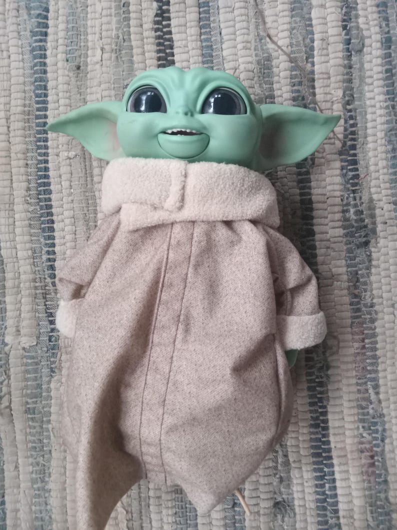 May include: A green plush toy with large eyes and a brown coat. The toy is smiling and has a large head.