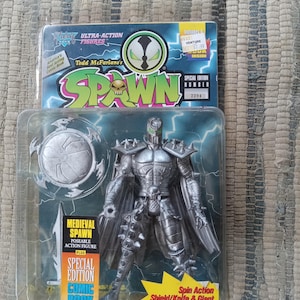 May include: A silver action figure of Spawn, a comic book character, in a medieval-style armor with a cape, holding a sword and shield. The figure is packaged in a plastic blister pack with a comic book included. The packaging features the character's name, "Spawn", and the words "Special Edition Number 2294".