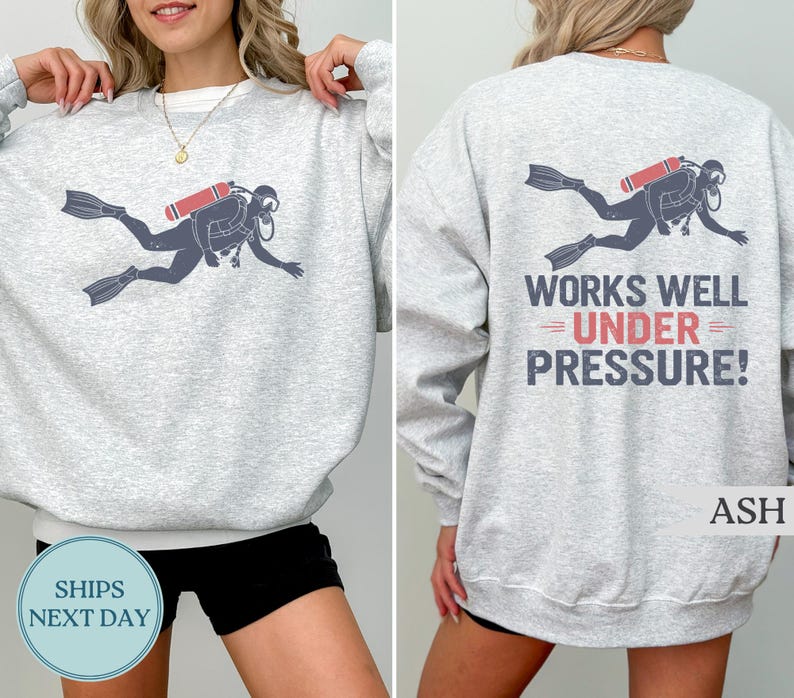 A woman wearing a gray sweatshirt with a graphic of a scuba diver and the text "WORKS WELL UNDER PRESSURE!" printed on the back.