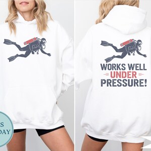 A white hoodie with a graphic of a scuba diver and the text "WORKS WELL UNDER PRESSURE!" printed on the back.