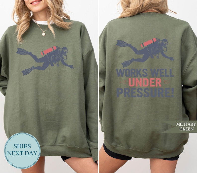 a woman wearing a green sweatshirt with a graphic of a scuba diver and the text "Works well under pressure!" printed on the back.
