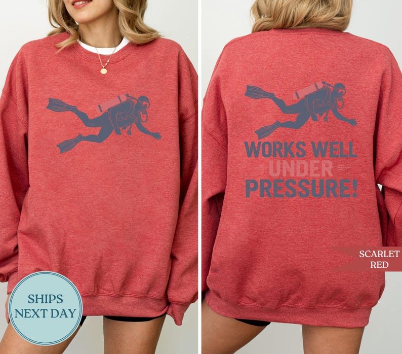 A red sweatshirt with a graphic of a scuba diver and the text "WORKS WELL UNDER PRESSURE!" printed on the back.