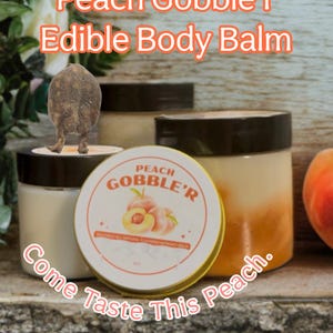 May include: Several jars of edible body balm are displayed, with the text "Peach Gobble'r Edible Body Balm" in orange. A round tin with the same branding is in front, with the words "Come Taste This Peach."
