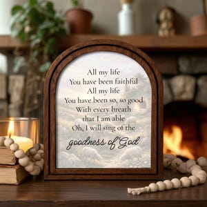May include: A wooden framed art piece with an arched top. The artwork features a pastoral scene with sheep and text that reads "All my life, You have been faithful...goodness of God."