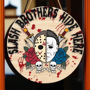 May include: Circular wooden sign with the text "SLASH BROTHERS HIDE HERE". The sign features a split face design, one side a hockey mask, the other a man's face. Includes roses, skulls, and knives.