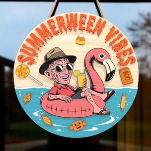 May include: Round wooden sign with the words "SUMMERWEEN VIBES" in orange. The sign features a cartoon character in a hat and sunglasses floating in a pink flamingo floatie, holding a drink. Candy and a "BOO" sign are also included.